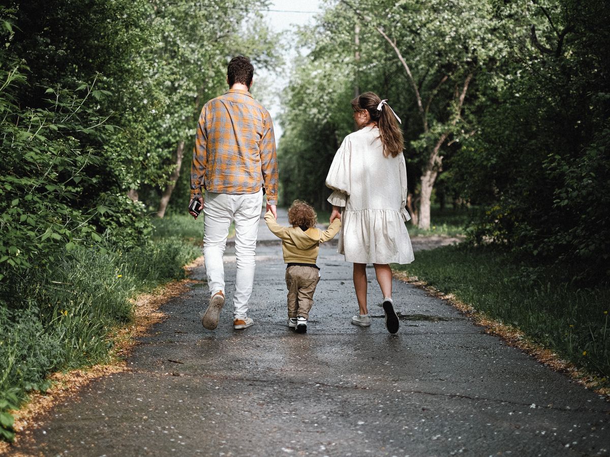 Um casal caminha ao ar livre com o filho pequeno em um parque arborizado